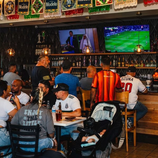 Lively Mexican sports bar filled with patrons, soccer playing on televisions, and Modelo banners decorating the bar area.