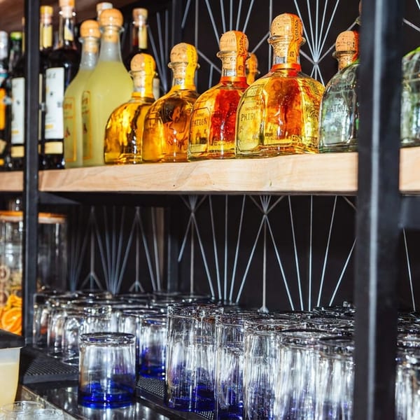 Shelves of colorful liquor bottles and rows of inverted drinking glasses line a stylish restaurant bar.
