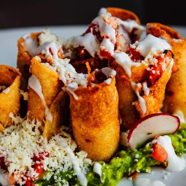 Golden rolled tacos topped with white sauce and cheese, served over lettuce with radish and tomato garnish.