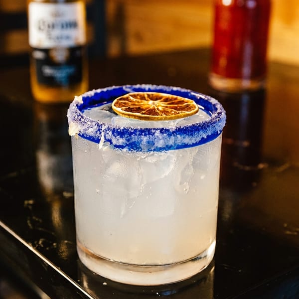Margarita with a blue salt rim, ice, and dried citrus garnish sits on a glossy bar counter.